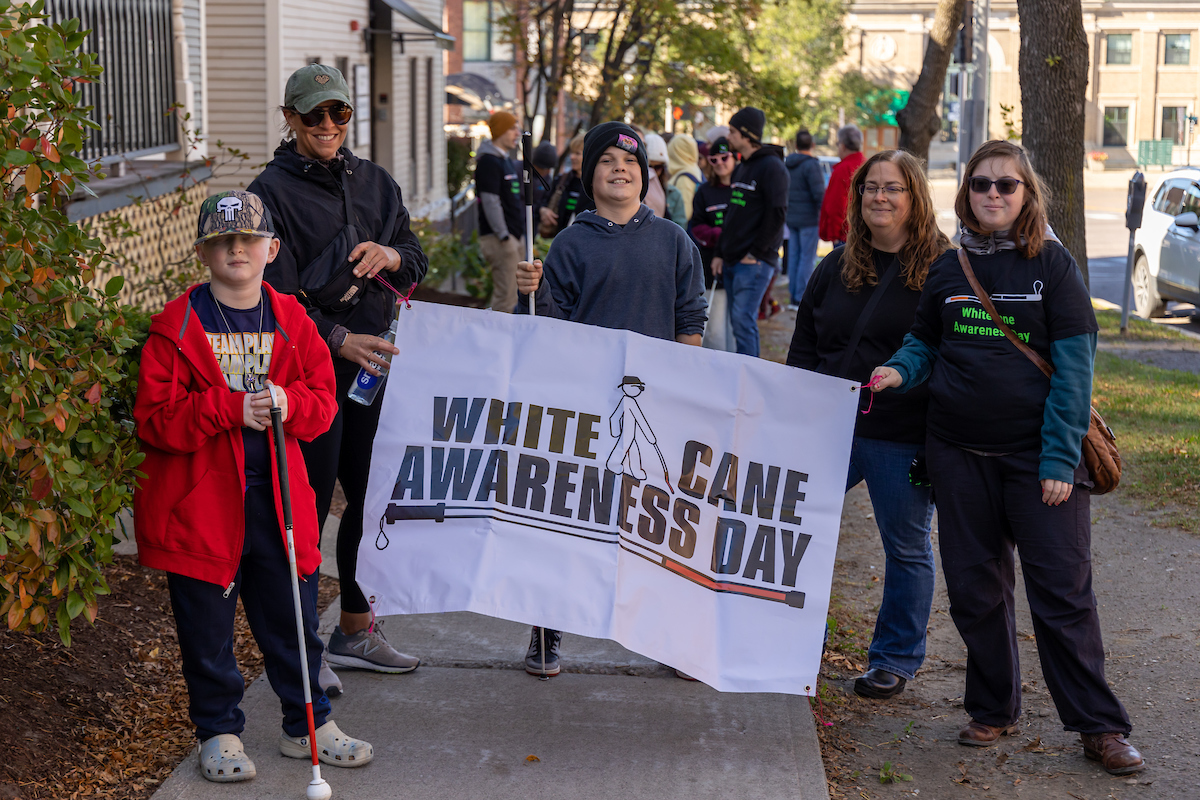 A group of five people pose on a sidewalk holding a 